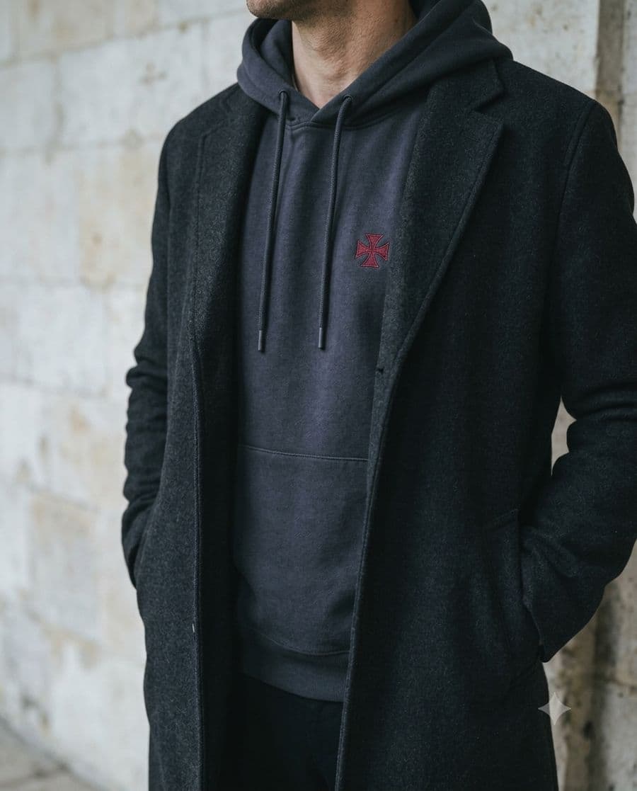 Charcoal hoodie with red cross worn under an open wool overcoat